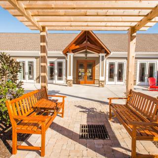 Outdoor seating area with wooden benches under a pergola leading to a building entrance.