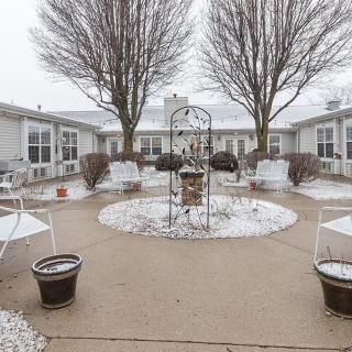 A snowy courtyard with outdoor seating surrounded by trees on an overcast day.