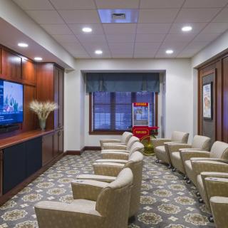 A well-furnished waiting room with rows of chairs facing a television, featuring elegant decor and indoor lighting.