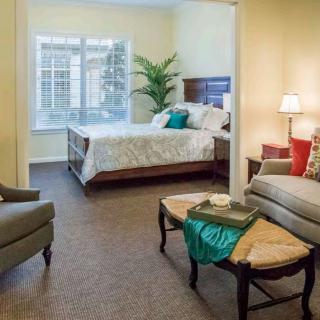 A cozy bedroom with a bed, armchairs, and a small table, styled with home decor elements.