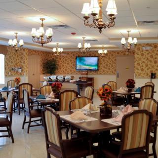 A well-decorated dining area with multiple tables, chairs, and chandeliers, featuring a mounted television on the wall.