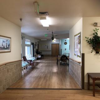A well-lit hallway with wooden flooring and seating areas, adorned with wall decorations and indoor plants.