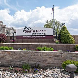 The entrance sign for Sierra Place Senior Living, surrounded by landscaped gardens and under a partly cloudy sky.