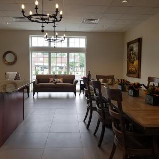 A well-lit dining area with a chandelier, tables and chairs, and a sofa near large windows.
