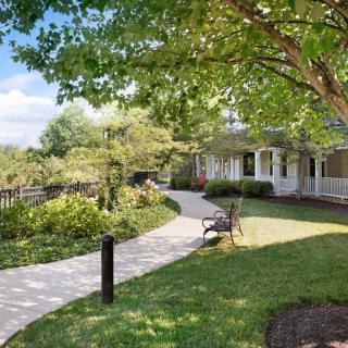 A serene garden pathway leading to a house, surrounded by trees and a well-maintained lawn.