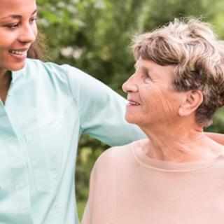 A caregiver and an elderly woman share a moment of support and companionship outdoors.