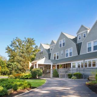 A large residential building with peaked roofs surrounded by trees and a landscaped garden on a sunny day.