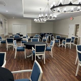 An empty dining or event space with neatly arranged tables and chairs, illuminated by chandeliers.