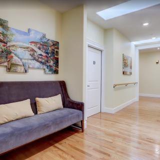 A well-lit hallway with a sofa and artwork on the walls, featuring wooden flooring and a skylight.