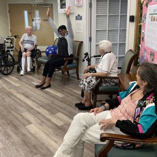 A group of elderly individuals engaging in a seated exercise session indoors.