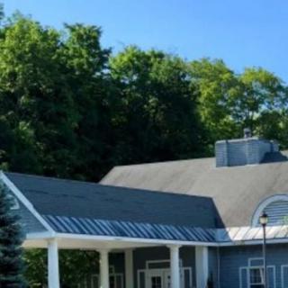 A modern blue house with a sloped roof surrounded by lush green trees under a clear blue sky.