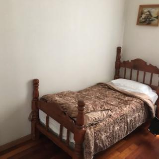 A cozy bedroom featuring a single wooden bed with a floral blanket and a small painting on the wall.