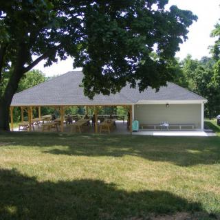An outdoor pavilion surrounded by trees and grass in a park setting.
