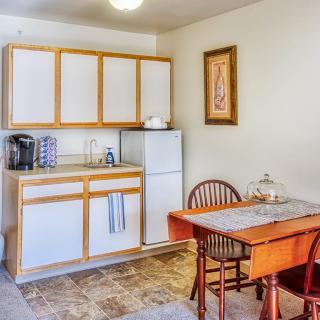 A compact kitchen and dining area featuring a small table and chairs, cabinets, a fridge, and a coffee maker.