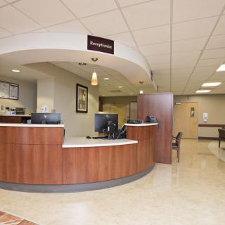 A hospital reception area with a curved desk and waiting room chairs.