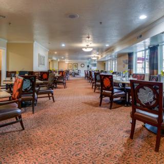 A spacious dining area with neatly arranged tables and chairs, featuring carpeted flooring and ambient lighting.