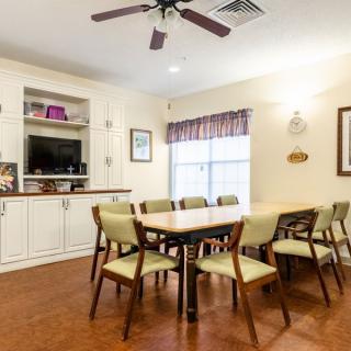 A cozy dining room with a long table and chairs, featuring built-in shelves, a ceiling fan, and a window allowing natural light.
