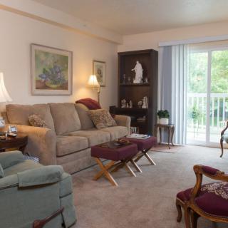 A cozy living room featuring a sofa, armchair, and coffee table, with decor including artwork and a shelf.