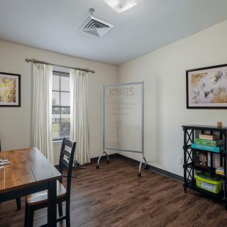 A simple office meeting room with a wooden table, chairs, whiteboard, and bookshelf.