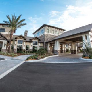 A modern residential building with a spacious driveway and palm trees.