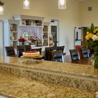 A cozy kitchen with a granite countertop, decorated with flowers and a cake in the dining area.