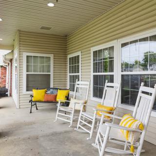 A cozy porch with white rocking chairs and a bench adorned with colorful cushions.