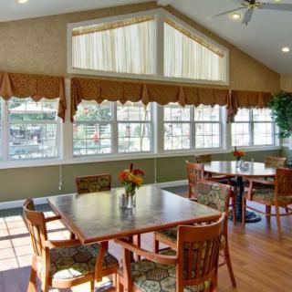 A well-lit dining area with tables and chairs, featuring large windows and curtains.