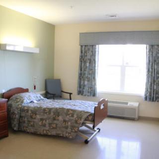 A spacious and well-lit hospital patient room with a bed, chair, and window.