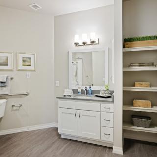 A modern bathroom with a white vanity, mirror, and open shelving.