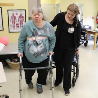 A healthcare professional assists an elderly woman using a walker during a rehabilitation session.