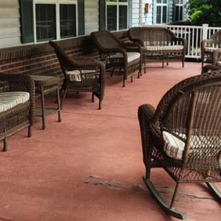 A patio with wicker furniture and rocking chairs arranged on a deck.