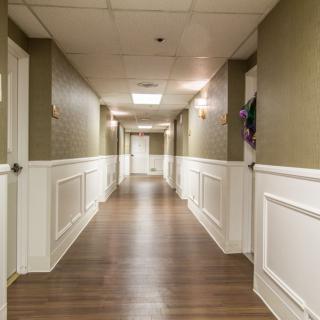 A long hallway with wood flooring and panelled walls, illuminated by ceiling lights.