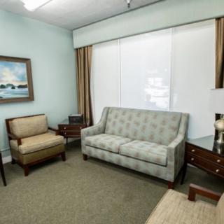 A cozy living room with a sofa and armchair, adorned with a painting and complemented by curtains.