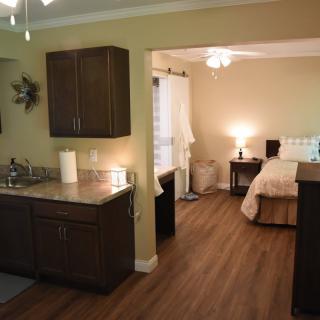 A cozy studio apartment with a kitchenette, wood flooring, and a well-lit bedroom area.