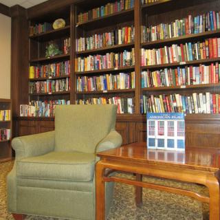A cozy reading area featuring a green armchair and a wooden table in front of a large bookshelf filled with books.
