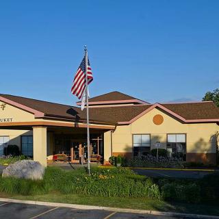A commercial building with an American flag in front, surrounded by a landscaped area and parking space.