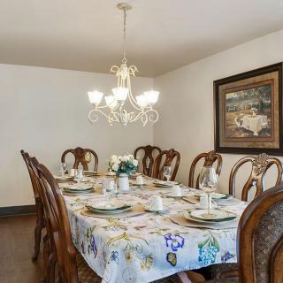 A dining room with an elegantly set table, surrounded by wooden chairs and lit by a chandelier.