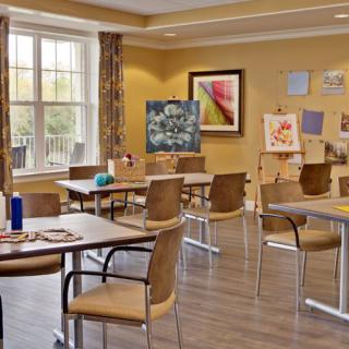 An art classroom with tables, chairs, and paintings displayed on easels.