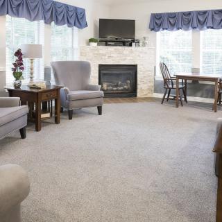 A cozy living room featuring armchairs, a fireplace, and a television, with large windows adorned by blue curtains.