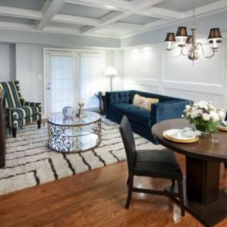 A stylish living room with a blue sofa, elegant coffee table, and adjacent dining area featuring a round table and chandelier.