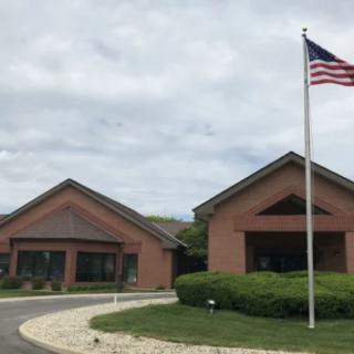 A brick building with a circular driveway and an American flag on a pole under a cloudy sky.