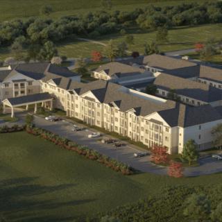 Aerial view of a large residential building surrounded by greenery and a parking lot.
