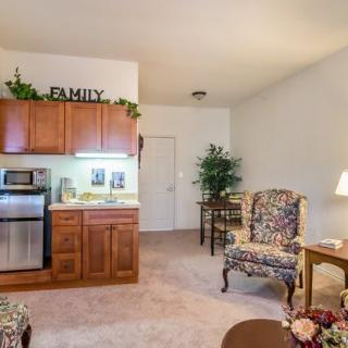 A cozy living area with a kitchenette, featuring wooden cabinets and floral-patterned armchairs.