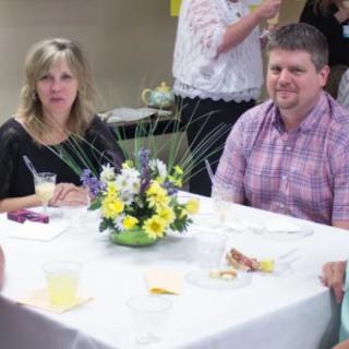 A group of people sitting at a table with a floral centerpiece during an indoor event.