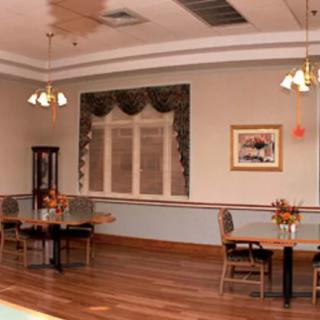A dining room with elegant chandeliers, several tables and chairs, and decorative elements including a painting and window drapes.