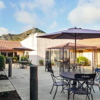 A patio area featuring several tables and chairs with umbrellas, set against a building and a blue sky.