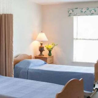A cozy bedroom with two twin beds, a bedside table with a lamp and flowers, and natural light coming through the window.
