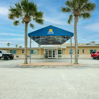 Entrance view of a building featuring a blue canopy and palm trees.