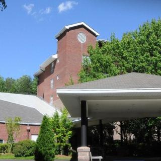A brick building with a canopy entrance surrounded by trees under a clear blue sky.