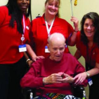 A group of caregivers in red shirts with an elderly person in a wheelchair.